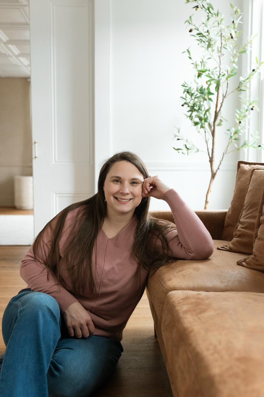 Kourtney Vanasse, DONA certified postpartum doula, seated in a warm, plant-filled home